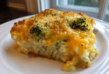 A close-up slice of creamy chicken broccoli rice casserole topped with melted cheddar cheese and breadcrumbs.