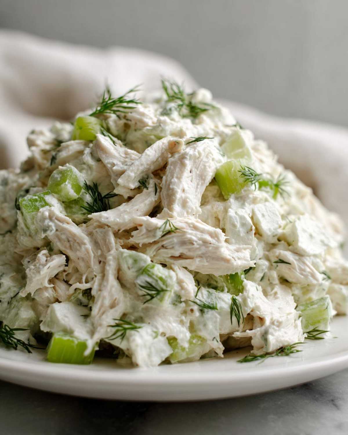 Close-up of a mound of creamy cottage cheese chicken salad mixed with chopped celery and topped with fresh dill.