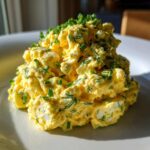 A mound of creamy, yellow egg salad recipe generously topped with freshly chopped green chives on a white plate.