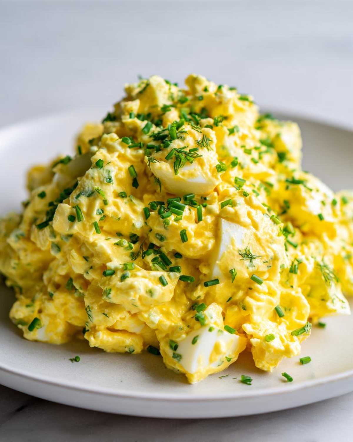 Close-up of a mound of creamy, yellow egg salad recipe generously garnished with chopped green chives.