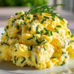 Close-up of a mound of creamy egg salad recipe garnished with fresh chopped chives and dill.