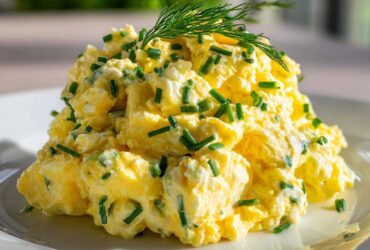 Close-up of a mound of creamy egg salad recipe garnished with fresh chopped chives and dill.