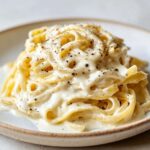 Close-up of fettuccine pasta generously coated in creamy homemade alfredo sauce and black pepper.