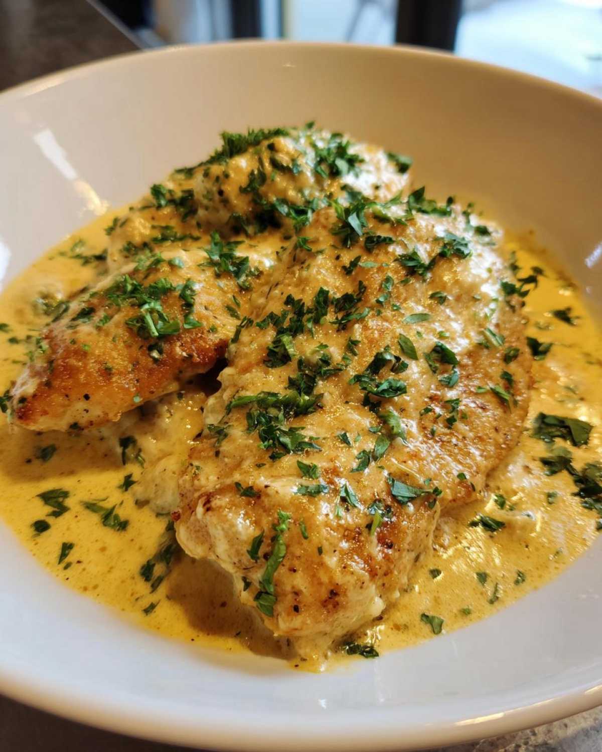 Close-up of pan-seared chicken breasts smothered in a rich, creamy lemon sauce and topped with fresh parsley.