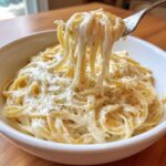 A fork lifting creamy fettuccine coated in rich Olive Garden Alfredo Sauce, topped with black pepper.