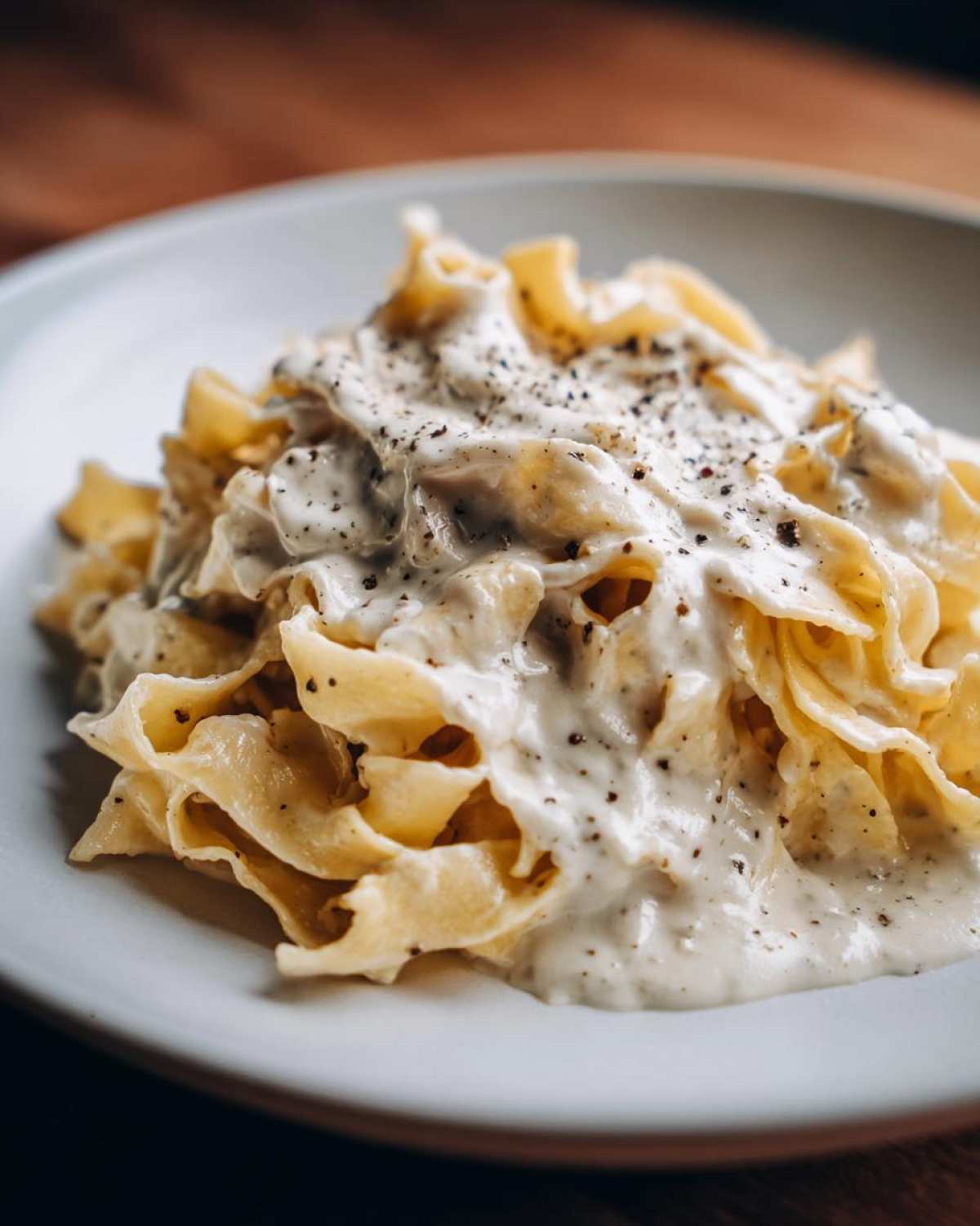 Close-up of wide egg noodles generously coated in rich homemade alfredo sauce and topped with cracked black pepper.