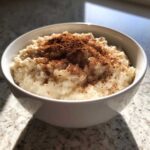 A close-up of creamy rice pudding in a white bowl, generously dusted with ground cinnamon.