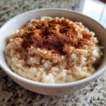 Close-up of creamy rice pudding served in a white bowl, generously dusted with cinnamon.
