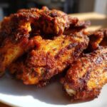 Close-up of a pile of golden-brown, seasoned, crispy baked chicken wings resting on a white plate.