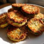Close-up of golden brown, crispy baked parmesan zucchini slices piled on a white plate.