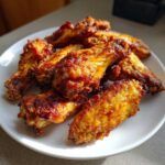 Close-up of several golden brown, crispy chicken wings piled on a white plate.