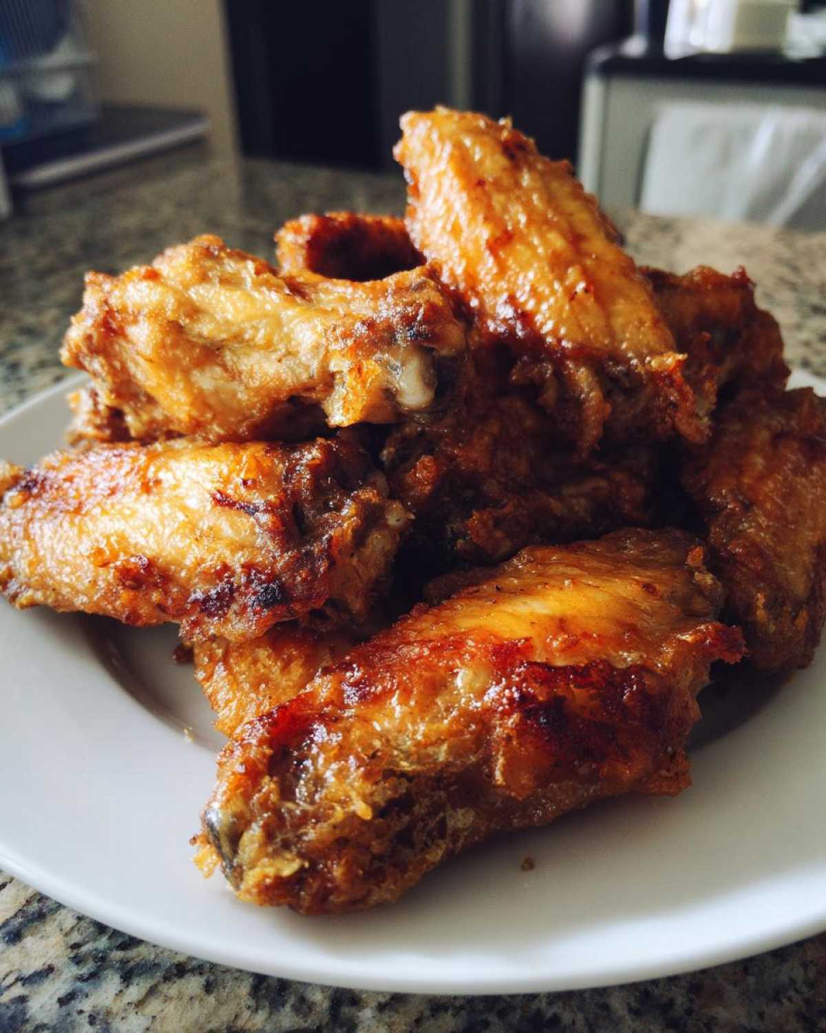 A close-up of several crispy, golden brown chicken wings piled high on a white plate.
