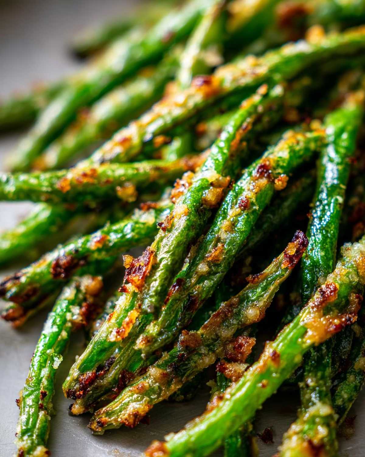 Close-up of perfectly roasted, crispy green beans coated in a savory, browned topping.