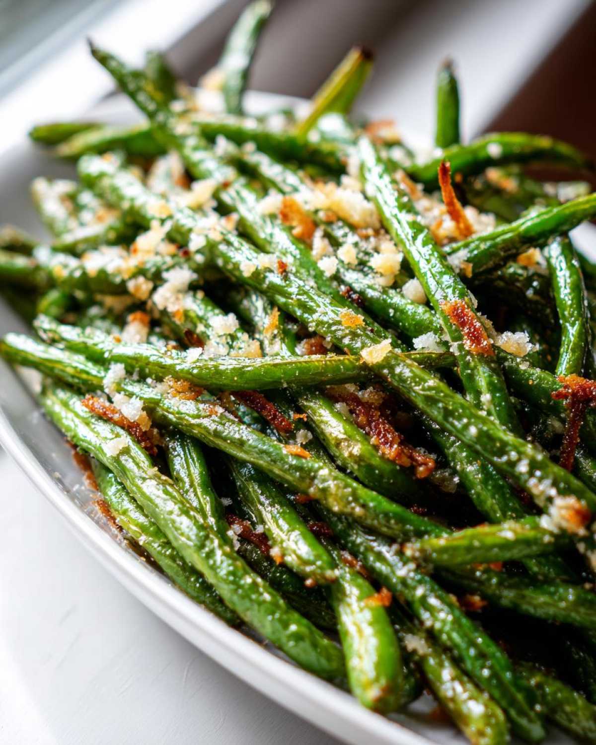 Close-up of bright green beans topped with crispy breadcrumbs and seasoning, ready to serve.