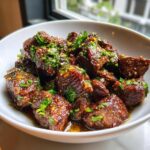 Close-up of tender, glazed crockpot steak bites topped generously with fresh chopped parsley and chili flakes.