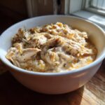 A white bowl filled with creamy, shredded crockpot white chicken chili, seasoned with herbs.