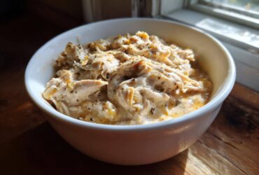 A white bowl filled with creamy, shredded crockpot white chicken chili, seasoned with herbs.