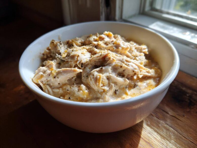 A white bowl filled with creamy, shredded crockpot white chicken chili, seasoned with herbs.