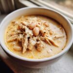 Close-up of a bowl filled with creamy crockpot white chicken chili, featuring shredded chicken and white beans.