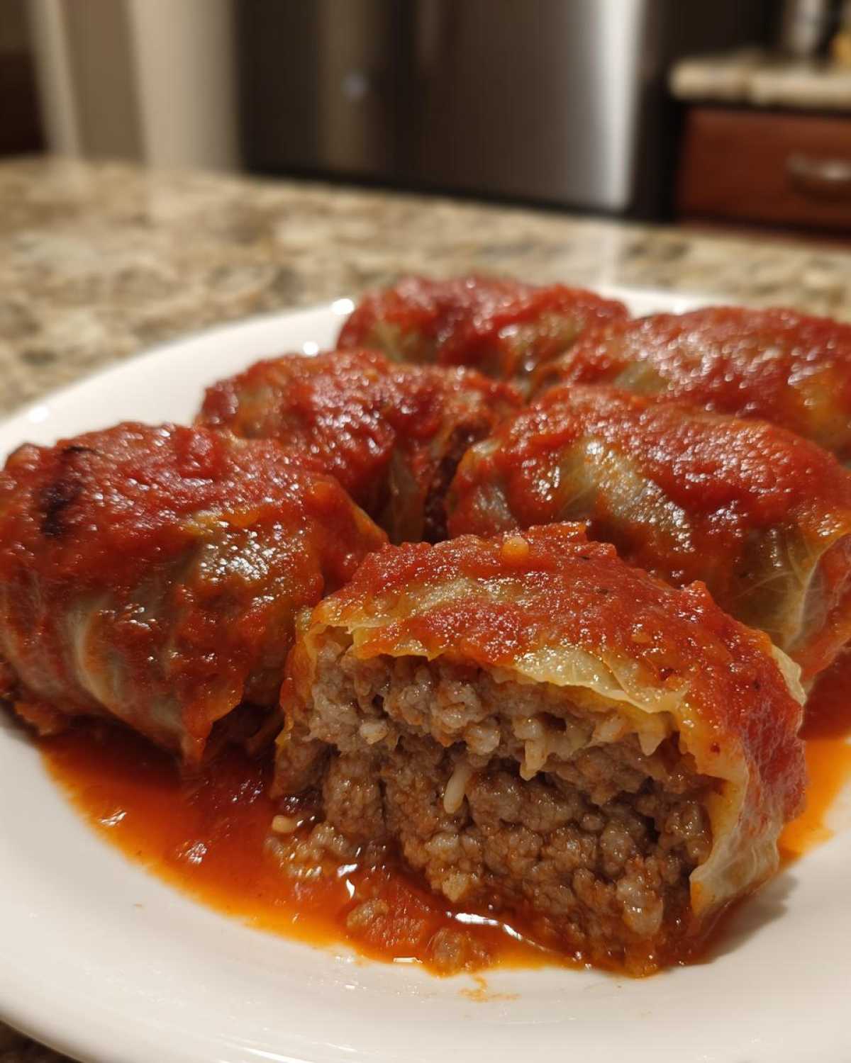Close-up of several cabbage rolls smothered in tomato sauce, showing the savory meat and rice filling inside one cut cabbage roll.