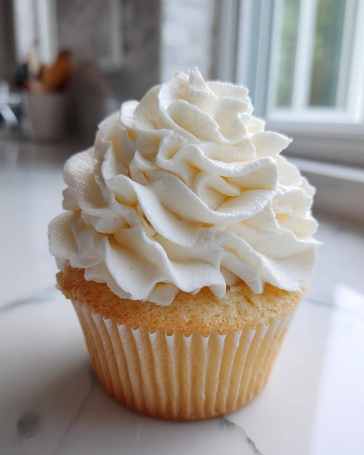 A close-up of a vanilla cupcake topped with perfectly piped swirls of creamy vanilla buttercream frosting.