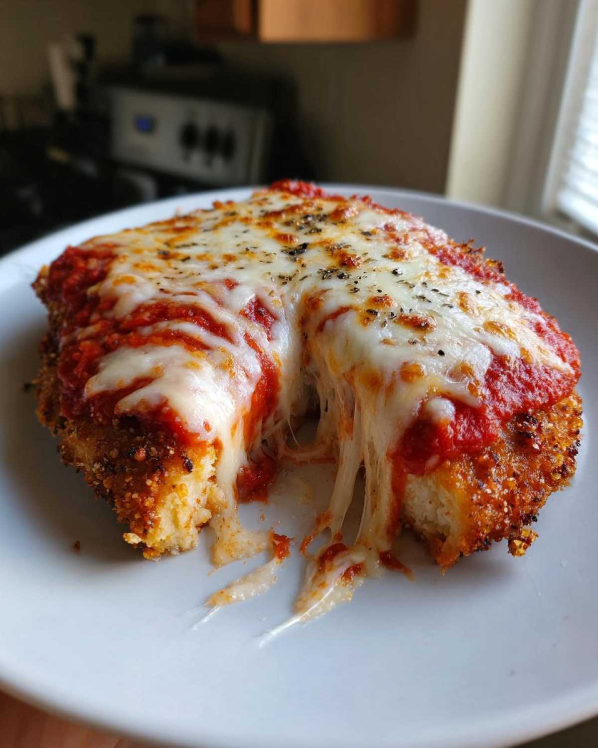 Close-up of Easy Chicken Parmesan with melted mozzarella cheese stretching as the cut piece is lifted.