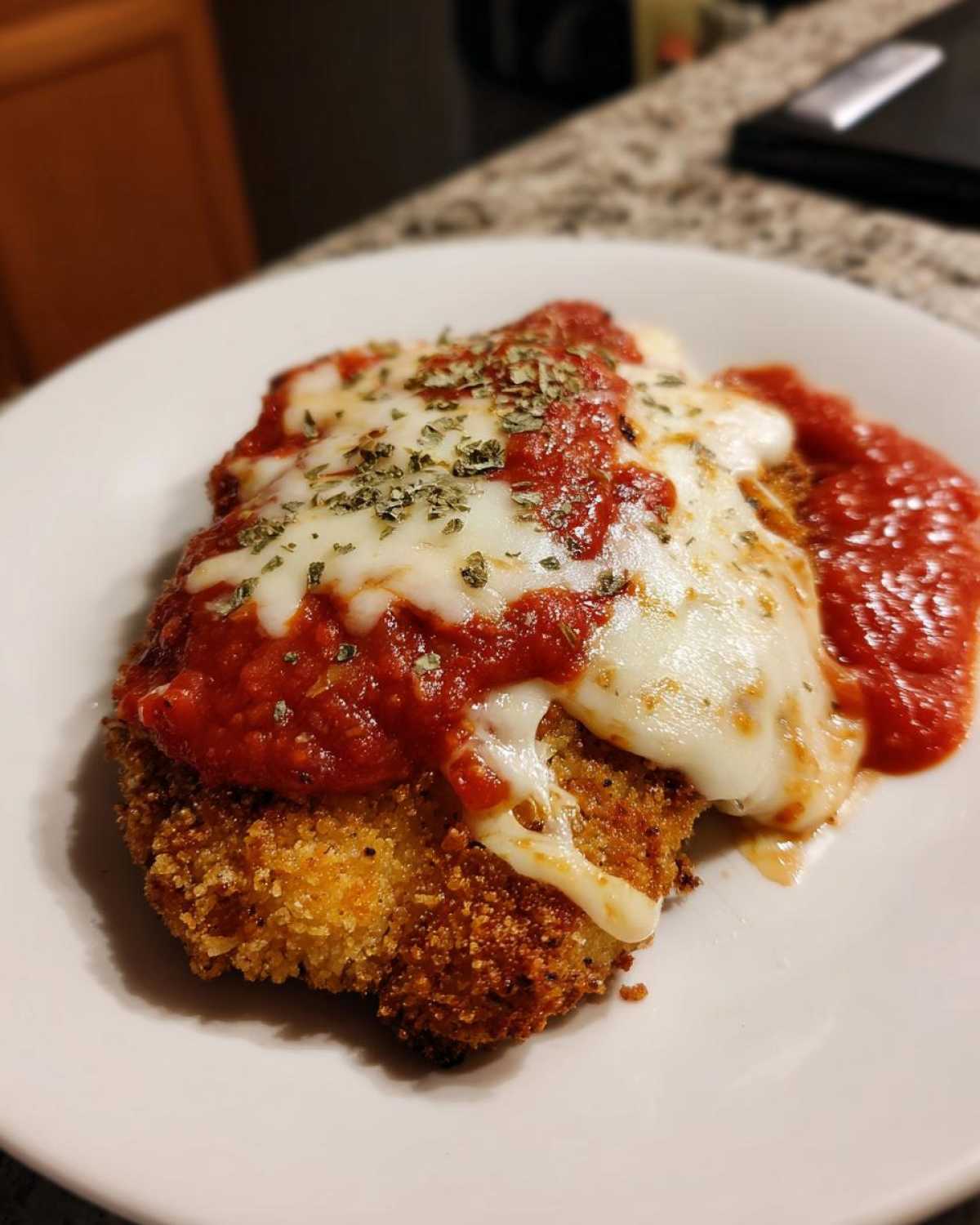 A close-up of a breaded cutlet topped with marinara sauce and melted mozzarella, representing Easy Chicken Parmesan.
