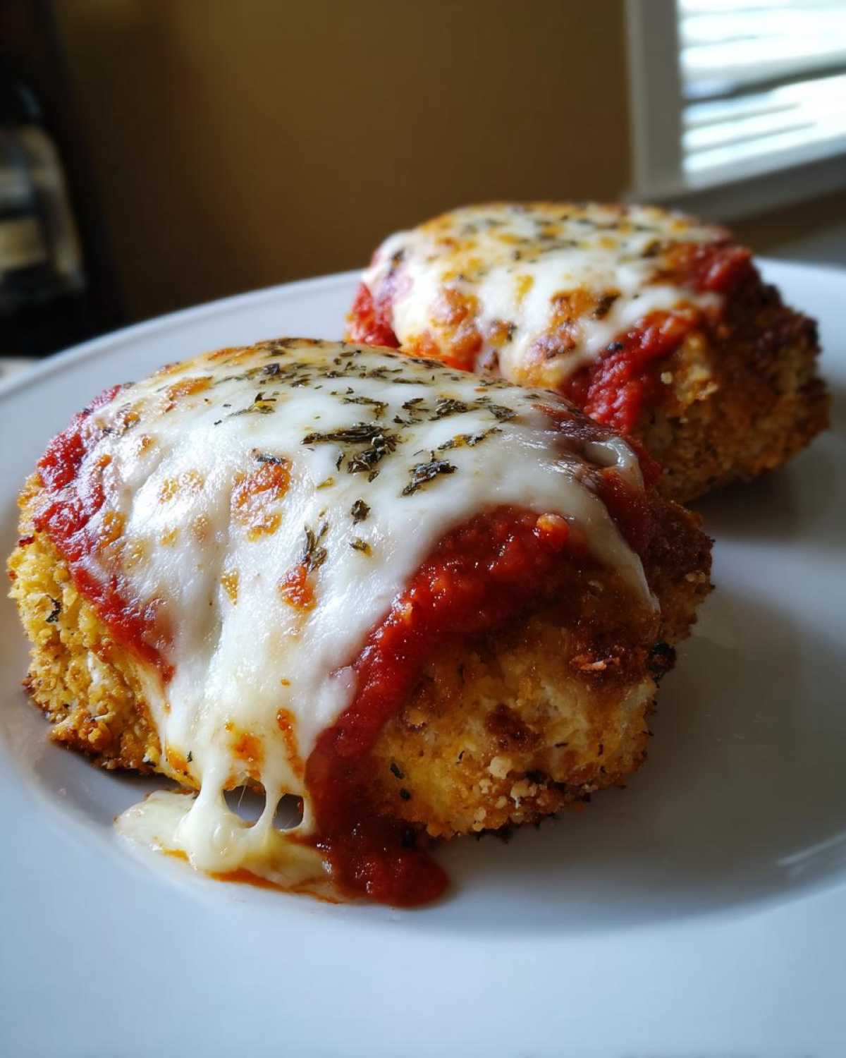 Two golden-brown, breaded chicken cutlets topped with marinara sauce and melted mozzarella cheese for Easy Chicken Parmesan.