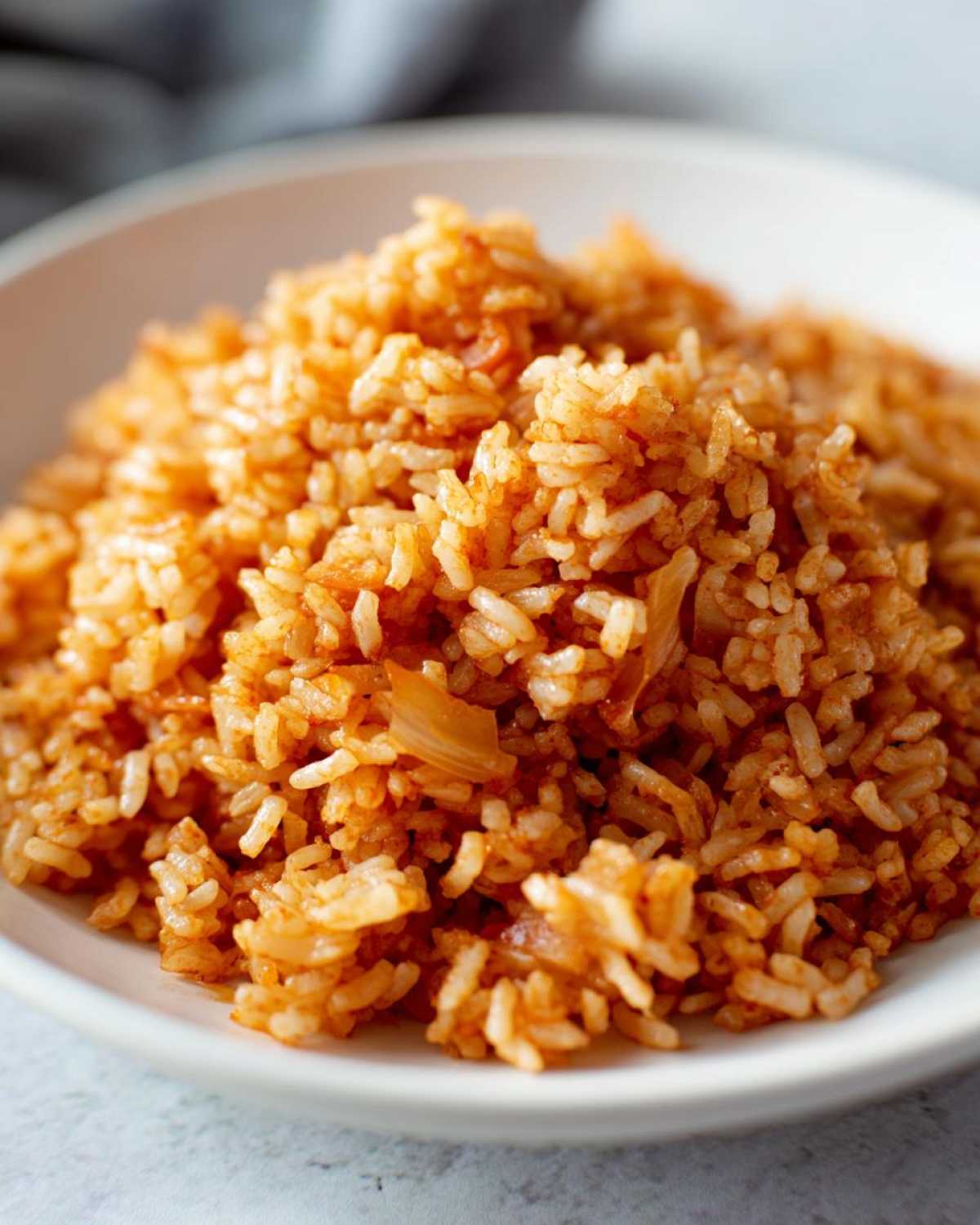 Close-up of fluffy, orange-red seasoned Spanish rice served in a white bowl.
