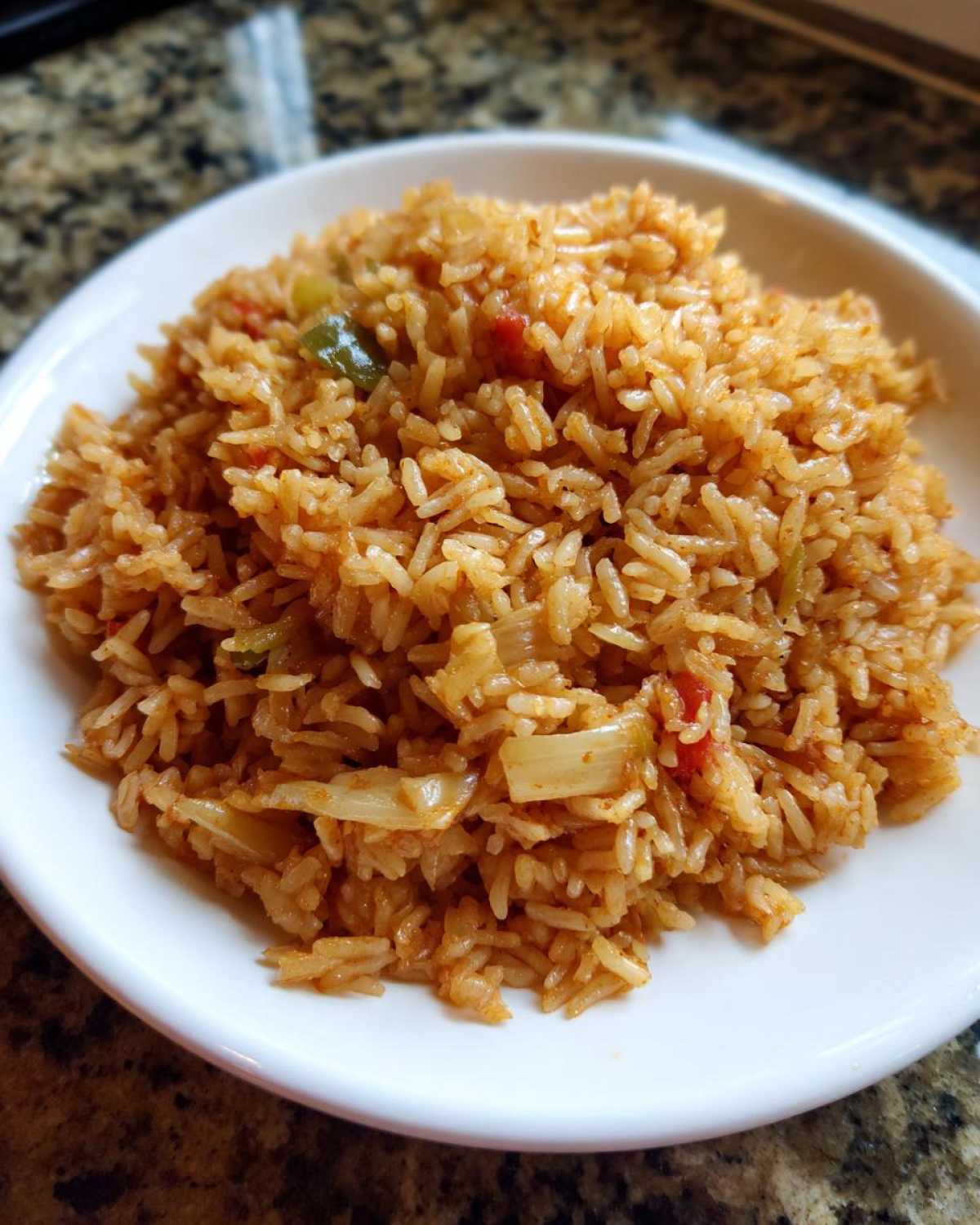 A close-up view of fluffy, seasoned Spanish rice mixed with visible pieces of onion and peppers served in a white bowl.