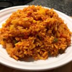 Close-up of a generous serving of vibrant, orange-red Spanish rice mixed with vegetables on a white plate.