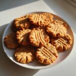 A close-up shot of a pile of freshly baked Easy Peanut Butter Cookies with classic fork cross-hatch marks on a white plate.