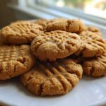 A close-up of several golden brown Easy Peanut Butter Cookies stacked on a white plate, showing classic crosshatch fork marks.