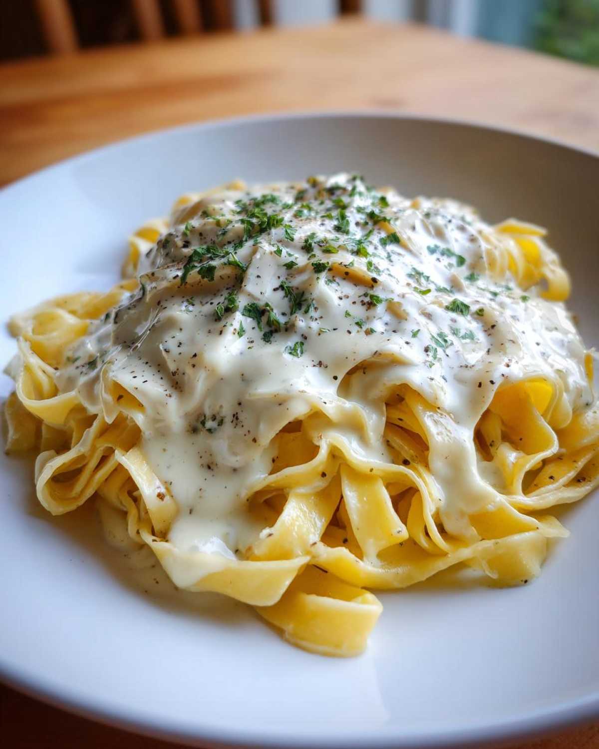 Close-up of fettuccine pasta generously coated in creamy homemade alfredo sauce, topped with black pepper and parsley.