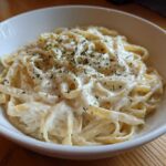 Close-up of fettuccine pasta coated in creamy Olive Garden Alfredo Sauce, topped with parsley.