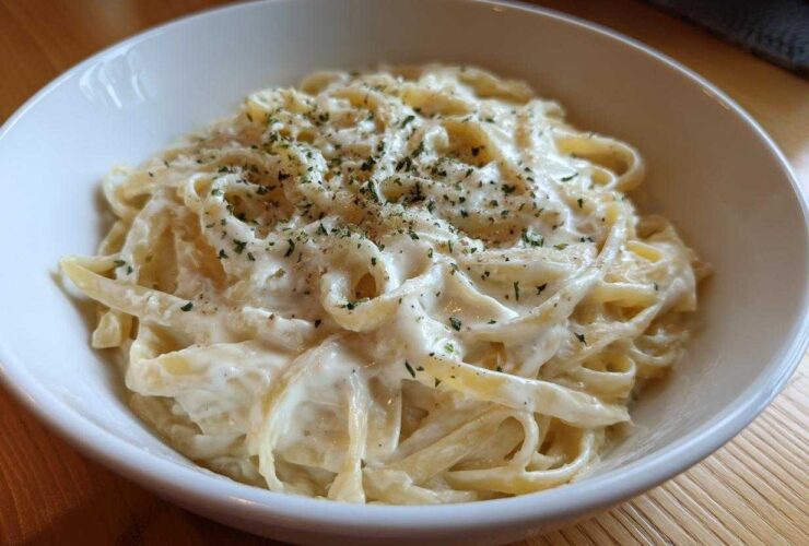 Close-up of fettuccine pasta coated in creamy Olive Garden Alfredo Sauce, topped with parsley.