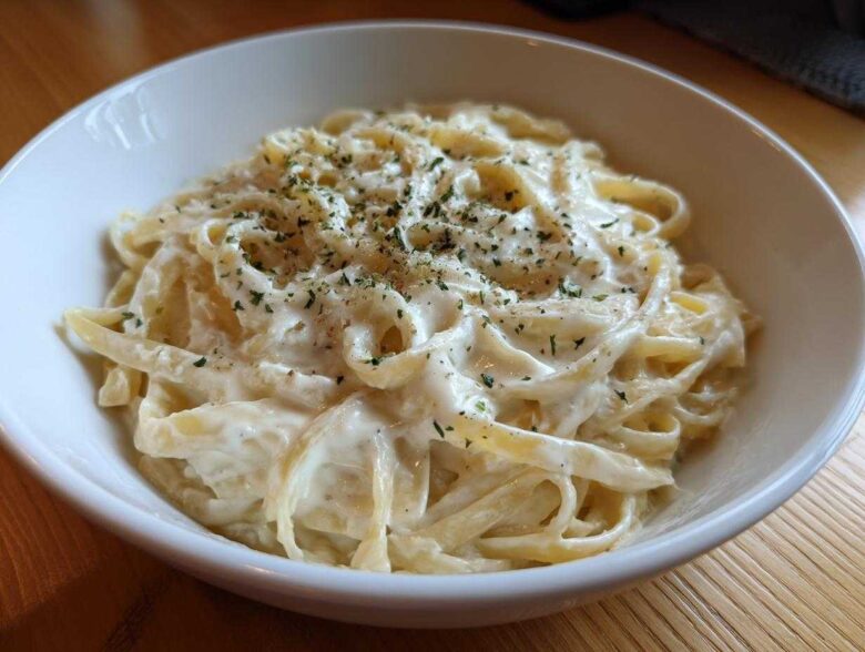Close-up of fettuccine pasta coated in creamy Olive Garden Alfredo Sauce, topped with parsley.