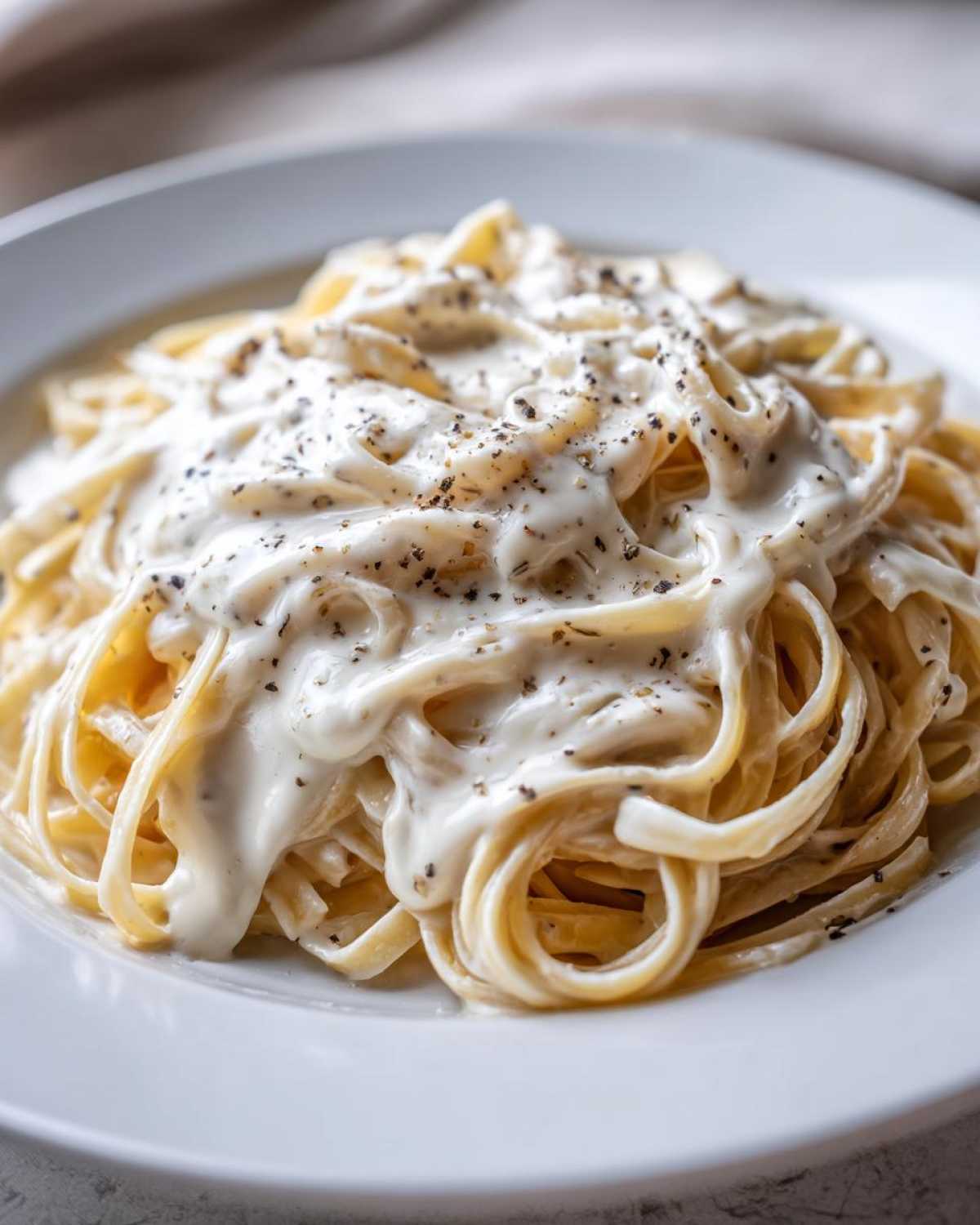 Close-up of fettuccine pasta generously coated in creamy homemade alfredo sauce and topped with cracked black pepper.