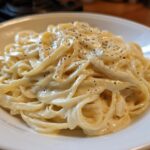 Close-up of fettuccine pasta generously coated in rich homemade alfredo sauce and topped with fresh black pepper.