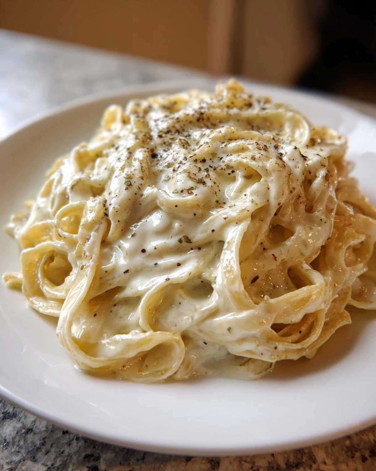 Close-up of fettuccine pasta generously coated in creamy homemade alfredo sauce and topped with black pepper.