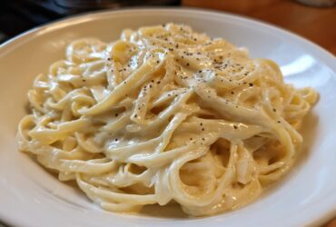 Close-up of fettuccine pasta generously coated in rich homemade alfredo sauce and topped with fresh black pepper.