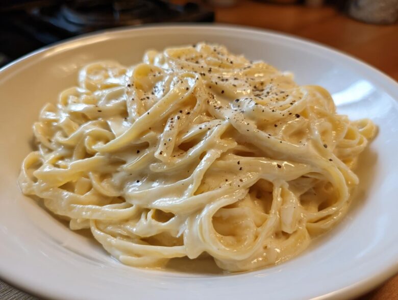 Close-up of fettuccine pasta generously coated in rich homemade alfredo sauce and topped with fresh black pepper.