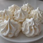 Five perfectly piped, white meringue cookies with sharp peaks arranged on a white plate.