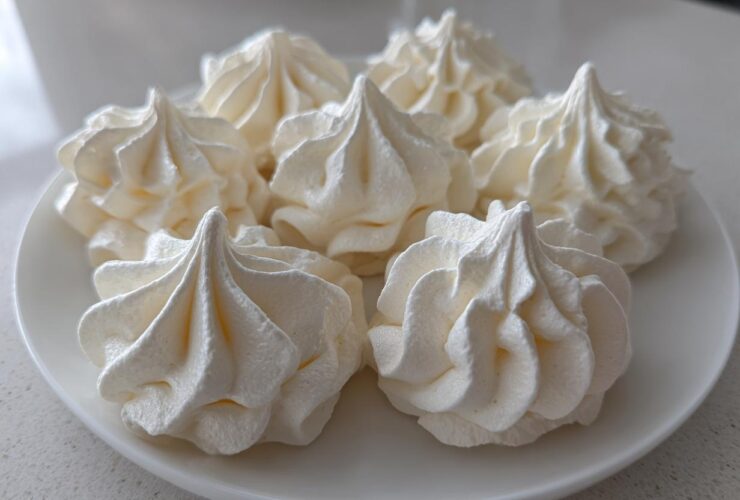 Five perfectly piped, white meringue cookies with sharp peaks arranged on a white plate.