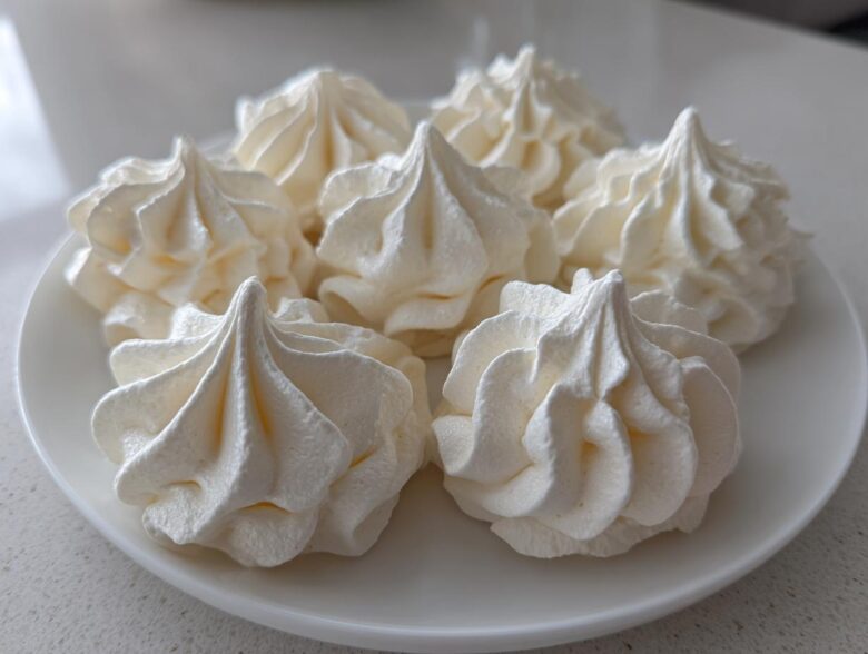 Five perfectly piped, white meringue cookies with sharp peaks arranged on a white plate.