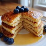 A stack of fluffy almond flour pancakes cut in half, drizzled with syrup and topped with fresh blueberries.