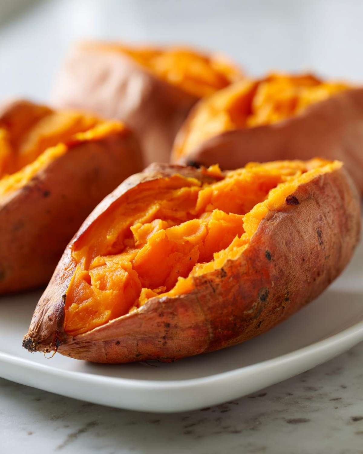 Close-up of a perfectly baked sweet potato split open, showing the bright orange, fluffy interior.