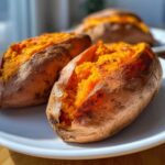 Close-up of two perfectly baked sweet potato halves with bright orange, fluffy insides on a white plate.