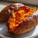 Close-up of two perfectly baked sweet potatoes, one split open revealing fluffy orange flesh.