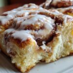 A close-up of a soft, fluffy cinnamon roll generously topped with white cream cheese icing.